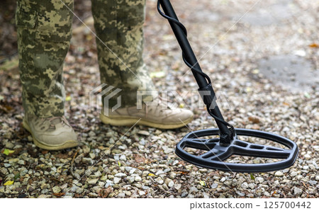A military sapper with a metal detector in the field. A Ukrainian explosive technician carries out demining work. A military sapper with a metal detector in the field. A Ukrainian explosive technician carries out demining work. 125700442