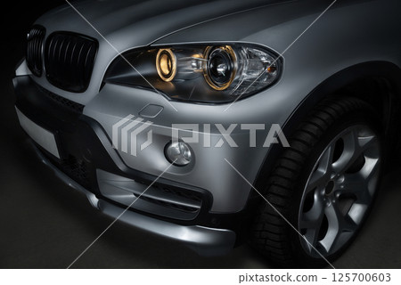 Close-up of the front headlight of a silver crossover. 125700603