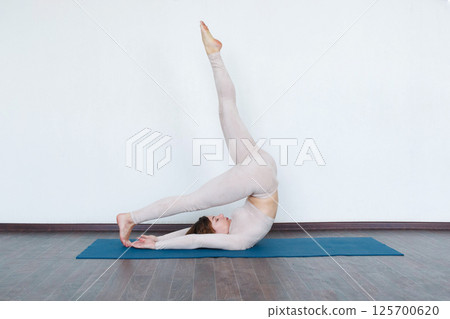 Beautiful girl practices kundalini yoga indoors in daylight. 125700620