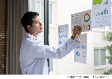 Doctor writing insights from data analysis on report at hospital 125700835