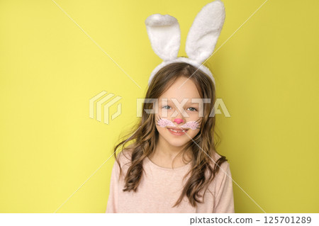 A sweet charming beautiful girl with curly hair, ears on head and a painted face in the guise of an Easter bunny A sweet charming beautiful girl with curly hair, ears on head and a painted face in the guise of an Easter bunny 125701289