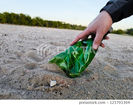 Closeup of volunteer hand putting plastic bottle inside plastic bag on the beach. A volunteer picks up a plastic bottle on the beach Closeup of volunteer hand putting plastic bottle inside plastic bag on the beach. A volunteer picks up a plastic bottle on the beach 125701304