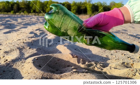 Closeup of volunteer hand in pink gloves putting plastic bottle inside plastic bag on the sand. A volunteer picks up a plastic bottle on the beach. Closeup of volunteer hand in pink gloves putting plastic bottle inside plastic bag on the sand. A volunteer picks up a plastic bottle on the beach. 125701306