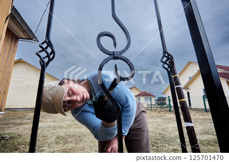 Painting work in local area, woman of about 50 years old applies black paint to metal railing of porch. 125701470