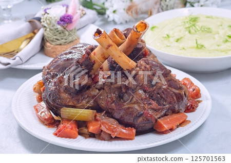 Delicious braised lamb shanks with vegetables served on a white plate, horizontal 125701563