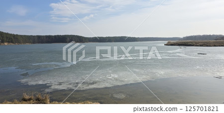 A partially frozen river under clear blue skies, surrounded by trees. Useful for nature, winter themes, environmental studies, or outdoor activities in marketing and design. 125701821