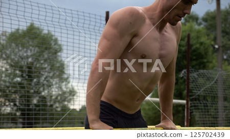 Male shirtless athlete doing push ups on parallel bars at nature. Strong sporty man exercising at sports ground. Young sportsman training hard outdoor. Concept of active sportive lifestyle. Slow mo 125702439