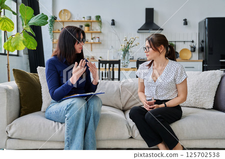 Female social worker interviewing middle aged woman, sitting together in living room Female social worker interviewing middle aged woman, sitting together in living room 125702538