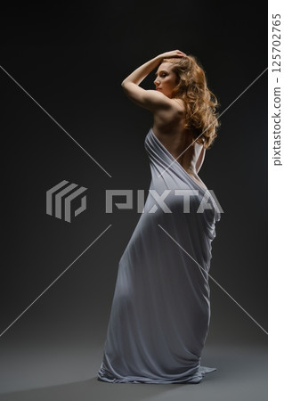 Sensual portrait of a woman elegantly draped in soft fabric at dusk 125702765