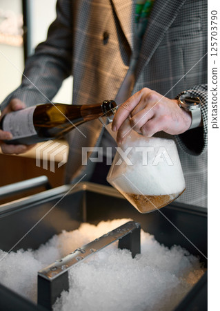 Champagne tasting, The sommelier pours sparkling wine from bottle into the decanter, sparkling wine bubbles, niche with ice 125703790