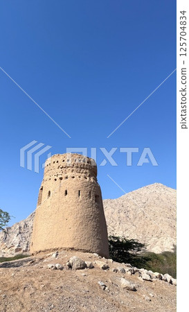 Ras Al Khaimah,UAE - March 29,2025 :Stone fortress anchors dry hillside, framed by endless azure sky, ancient architecture exudes timeless dignity and invites discovery, landmark, tourist attraction. 125704834