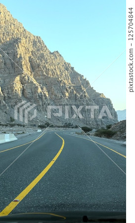Curved highway winds gracefully between canyon cliffs, road alignment flows like ribbon, sharp rocks cast strong shadows as travelers follow path into raw, sculpted wilderness. 125704844