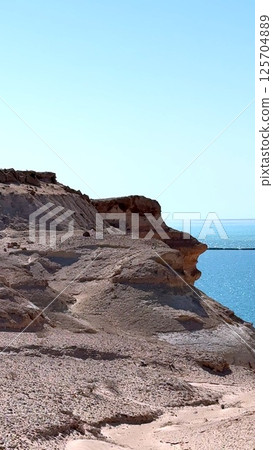 Rocky cliff towering over turquoise waters, revealing dramatic landscape within Ras Mohamed National Park, highlighting rugged coastline and pristine natural environment in Egypt 125704889