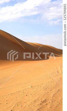 Sharp dune wall rises steep and smooth, edge cuts through glowing horizon as morning light draws golden line across untouched sand, surreal beauty forms minimalist tourist attraction. Sharp dune wall rises steep and smooth, edge cuts through glowing horizon as morning light draws golden line across untouched sand, surreal beauty forms minimalist tourist attraction. 125704891