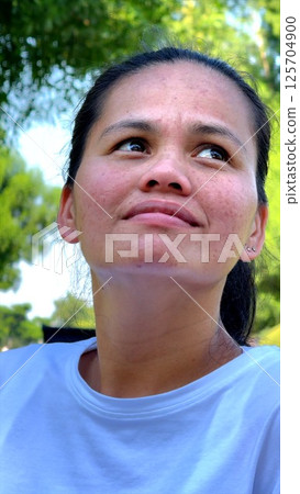 Woman with upward gaze appears determined bathed in natural light. Expression suggests purpose strength set against green surroundings emphasizing resilience and ambition. Concept Inner strength. 125704900