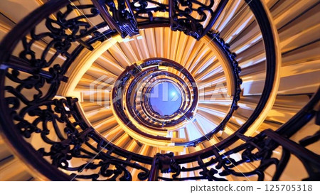 Multiple perspectives of an elegant spiral staircase winding upwards, its dark wooden handrail contrasting with cream colored steps, leading eye towards gently illuminated ceiling Multiple perspectives of an elegant spiral staircase winding upwards, its dark wooden handrail contrasting with cream colored steps, leading eye towards gently illuminated ceiling 125705318