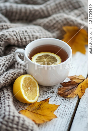 A cozy scene featuring a cup of tea with a lemon slice, surrounded by a knitted blanket and autumn leaves. A cozy scene featuring a cup of tea with a lemon slice, surrounded by a knitted blanket and autumn leaves. 125705489