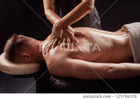 Close-up of professional deep tissue back massage on male client in wellness spa, hands applying firm pressure. Close-up of professional deep tissue back massage on male client in wellness spa, hands applying firm pressure. 125706378