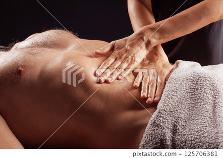 Therapist performing abdominal massage on male client to relieve tension and support digestive wellness. 125706381