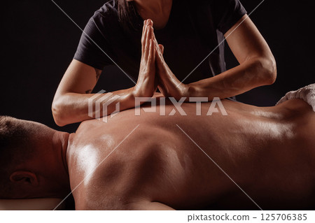 Close-up of therapist pressing palms together on man's back during deep tissue massage therapy for muscle relief. Close-up of therapist pressing palms together on man's back during deep tissue massage therapy for muscle relief. 125706385