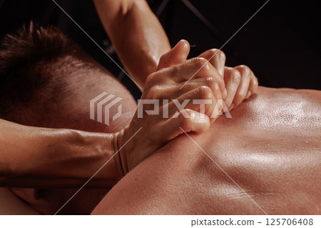 Close-up of deep tissue massage on a man's back, therapist applying intense pressure with clenched hands. Close-up of deep tissue massage on a man's back, therapist applying intense pressure with clenched hands. 125706408