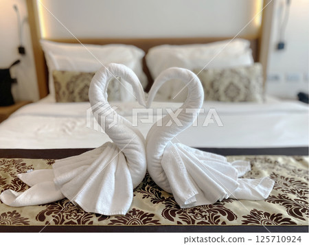 Romantic swan towel art arranged in a heart shape on a bed in a luxury hotel room, symbolizing love and hospitality blurred background. Romantic swan towel art arranged in a heart shape on a bed in a luxury hotel room, symbolizing love and hospitality blurred background. 125710924