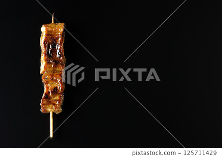Grilled eel skewers photographed against a black background 125711429