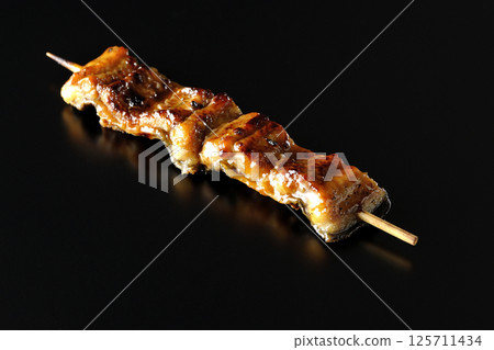 在黑色背景下拍攝的烤鰻魚串 在黑色背景下拍攝的烤鰻魚串 125711434