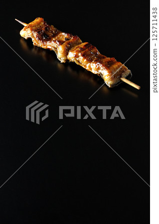 在黑色背景下拍攝的烤鰻魚串 在黑色背景下拍攝的烤鰻魚串 125711438