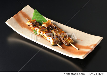 在黑色背景下拍攝的烤鰻魚串 在黑色背景下拍攝的烤鰻魚串 125711698