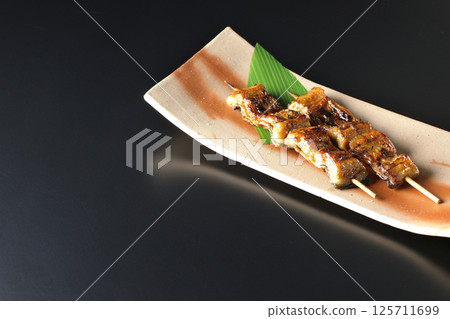 Grilled eel skewers photographed against a black background 125711699
