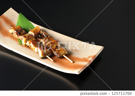 Grilled eel skewers photographed against a black background 125711700