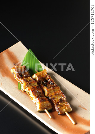 Grilled eel skewers photographed against a black background Grilled eel skewers photographed against a black background 125711702