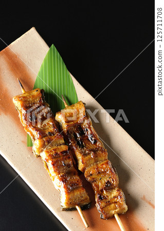 在黑色背景下拍攝的烤鰻魚串 在黑色背景下拍攝的烤鰻魚串 125711708