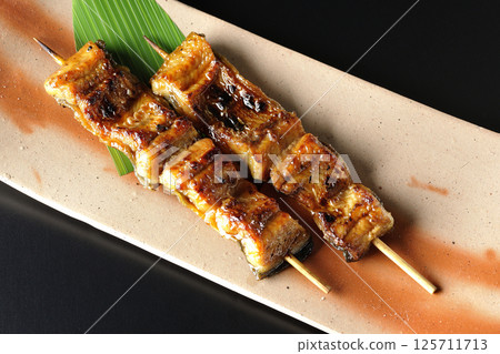 Grilled eel skewers photographed against a black background 125711713