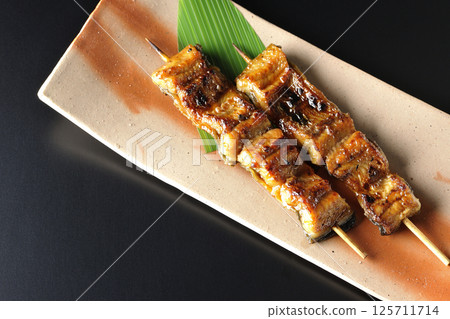 Grilled eel skewers photographed against a black background Grilled eel skewers photographed against a black background 125711714