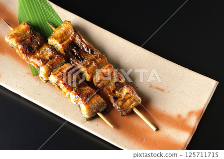 Grilled eel skewers photographed against a black background Grilled eel skewers photographed against a black background 125711715