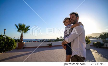 Father and child hugging in front of a landscape 125711950