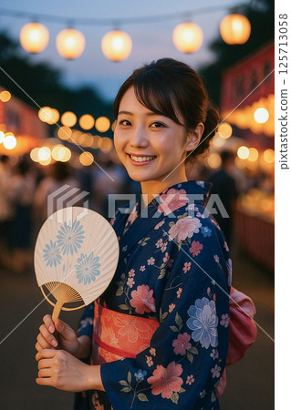 A woman in a yukata enjoys a summer festival with a fan 125713058