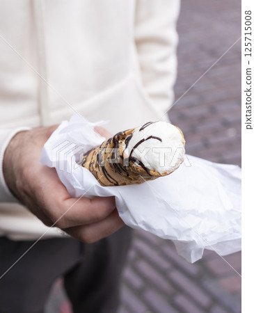 Hands Holding Cannoli Dessert, Traditional Sicilian Pastry, Tube-shaped Shell Of Fried Pastry Dough, Filled With A Sweet, Creamy Filling Containing Ricotta Cheese. Man Holds Street Food. Vertical. Hands Holding Cannoli Dessert, Traditional Sicilian Pastry, Tube-shaped Shell Of Fried Pastry Dough, Filled With A Sweet, Creamy Filling Containing Ricotta Cheese. Man Holds Street Food. Vertical. 125715008