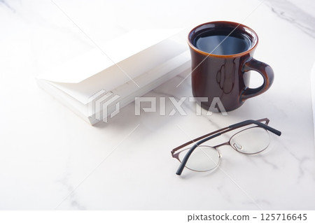 Image of a book, glasses and a coffee mug on a white table, enjoying reading while drinking coffee Image of a book, glasses and a coffee mug on a white table, enjoying reading while drinking coffee 125716645