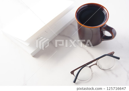 Image of a book, glasses and a coffee mug on a white table, enjoying reading while drinking coffee Image of a book, glasses and a coffee mug on a white table, enjoying reading while drinking coffee 125716647