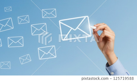 A hand draws a digital envelope icon with chalk on a blue background with floating email symbols. 125719588
