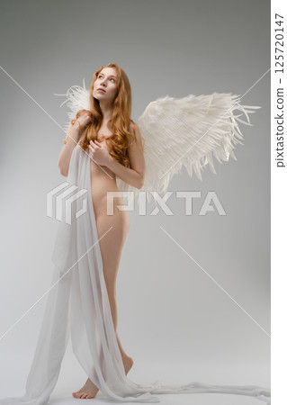 Naked woman with wings and body art poses in minimalistic studio 125720147