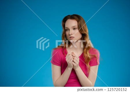 Woman expressing emotion while posing in a studio with a solid blue backdrop during a photo session 125720152