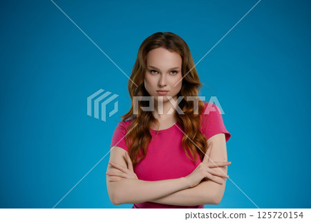 Confident woman poses with arms crossed against a vibrant blue backdrop in a studio setting 125720154