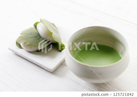 Kashiwa mochi and Cup of fresh matcha tea. Japanese sweet from mochi or rice cake and sweet red bean paste filling surrounded with Kashiwa or Oak leaf . Kashiwa mochi and Cup of fresh matcha tea. Japanese sweet from mochi or rice cake and sweet red bean paste filling surrounded with Kashiwa or Oak leaf . 125721842