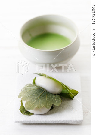 Kashiwa mochi and Cup of fresh matcha tea. Japanese sweet from mochi or rice cake and sweet red bean paste filling surrounded with Kashiwa or Oak leaf . Kashiwa mochi and Cup of fresh matcha tea. Japanese sweet from mochi or rice cake and sweet red bean paste filling surrounded with Kashiwa or Oak leaf . 125721843