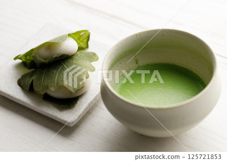 Kashiwa mochi and Cup of fresh matcha tea. Japanese sweet from mochi or rice cake and sweet red bean paste filling surrounded with Kashiwa or Oak leaf . Kashiwa mochi and Cup of fresh matcha tea. Japanese sweet from mochi or rice cake and sweet red bean paste filling surrounded with Kashiwa or Oak leaf . 125721853