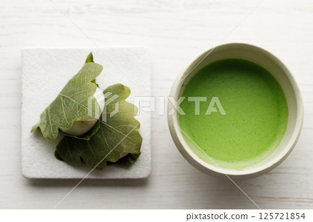 Kashiwa mochi and Cup of fresh matcha tea. Japanese sweet from mochi or rice cake and sweet red bean paste filling surrounded with Kashiwa or Oak leaf . Kashiwa mochi and Cup of fresh matcha tea. Japanese sweet from mochi or rice cake and sweet red bean paste filling surrounded with Kashiwa or Oak leaf . 125721854